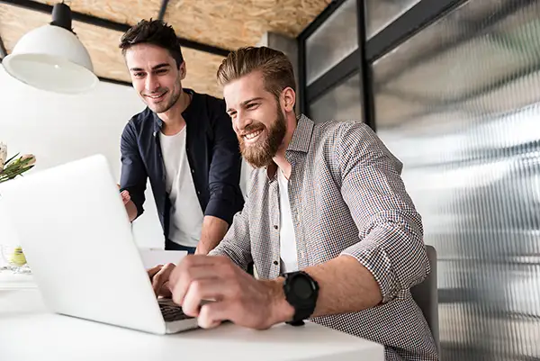 Zwei junge Männer arbeiten gemeinsam an einem Laptop – Teamwork und kreative Zusammenarbeit bei Werk Media - Karriere & Jobs