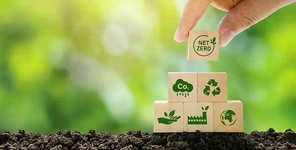 Digitale Nachhaltigkeit: Hand setzt Baustein mit Net-Zero-Symbol auf Stapel aus CO₂-Reduktion, Recycling, nachhaltige Produktion und Klimaschutz