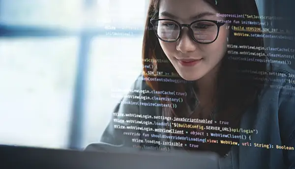 Frau mit Brille programmiert auf Laptop – Codezeilen im Vordergrund - Individuelle Webentwicklung